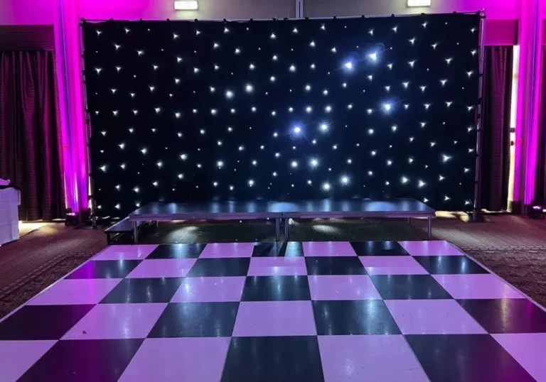 Empty marquee dance floor with a black and white checkered pattern, leading up to a stage with a star-lit backdrop in a dimly lit room.