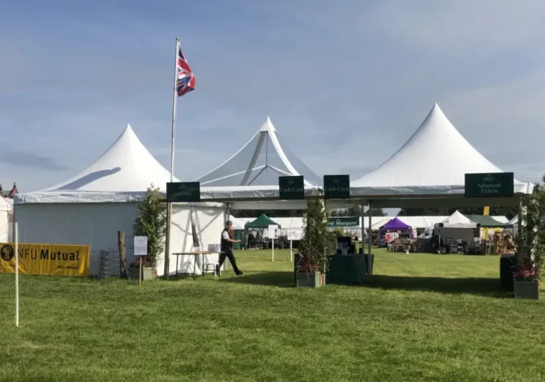 Two large festival marquees by Melody Corporation with peaks at an outdoor event, featuring banners of "nfu mutual" and the UK flag flying atop a flagpole on a sunny day.