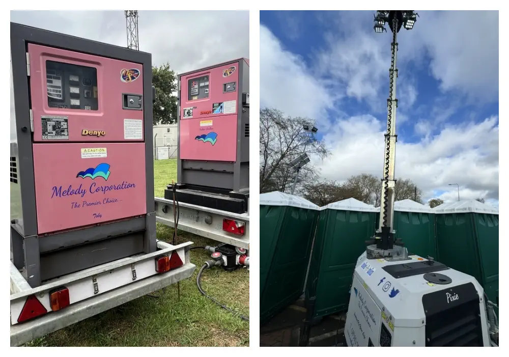 Portable restroom rental trucks parked on grass beside a tall lighting tower, equipped with power and lighting solutions by Melody Corporation, under a cloudy sky.