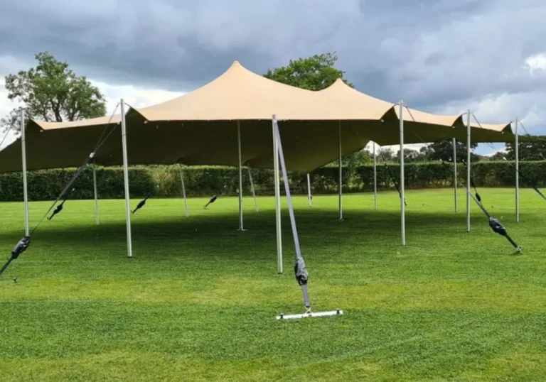 Large beige stretch tent from Melody Corporation set up on a grassy field with overcast skies above.