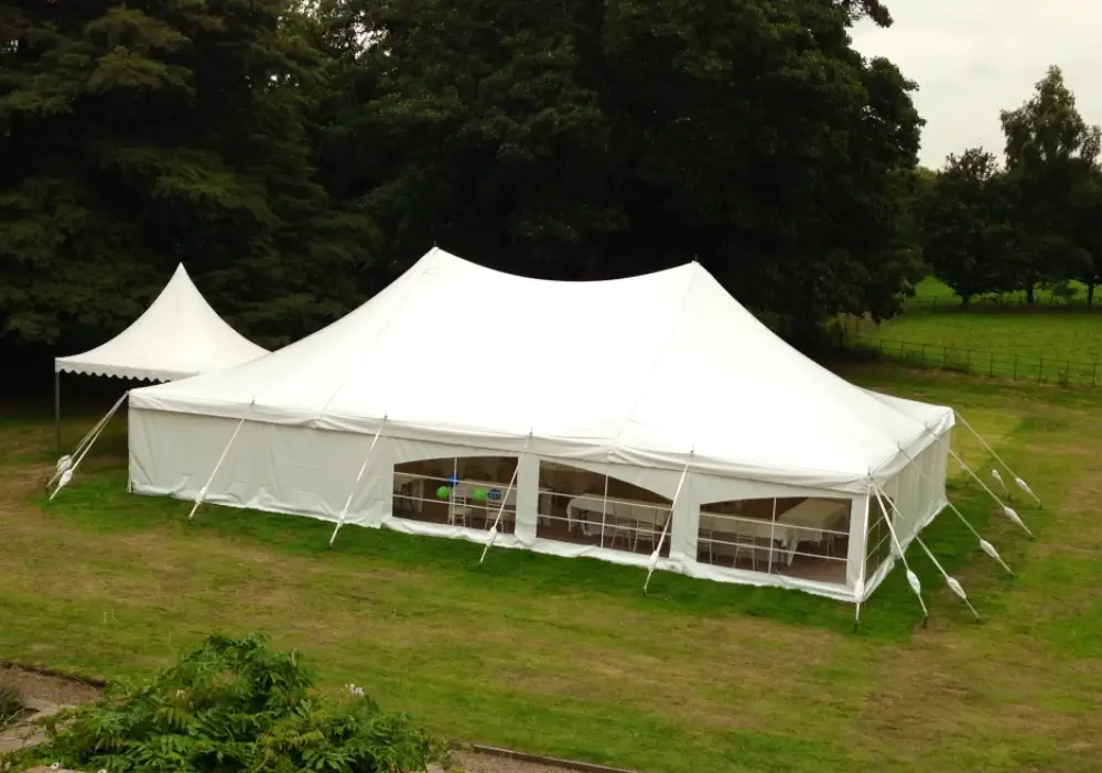 Large white traditional marquee of Melody Corporation with open sides set up on a grassy field surrounded by trees.
