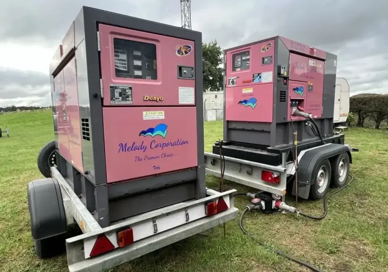 Two pink industrial generators labeled "Melody Corporation" are mounted on trailers in a grassy area, looking as if they're ready to power up a grand marquee event. One trailer has hoses connected, and both showcase branded stickers and control panels, complete with all necessary accessories.